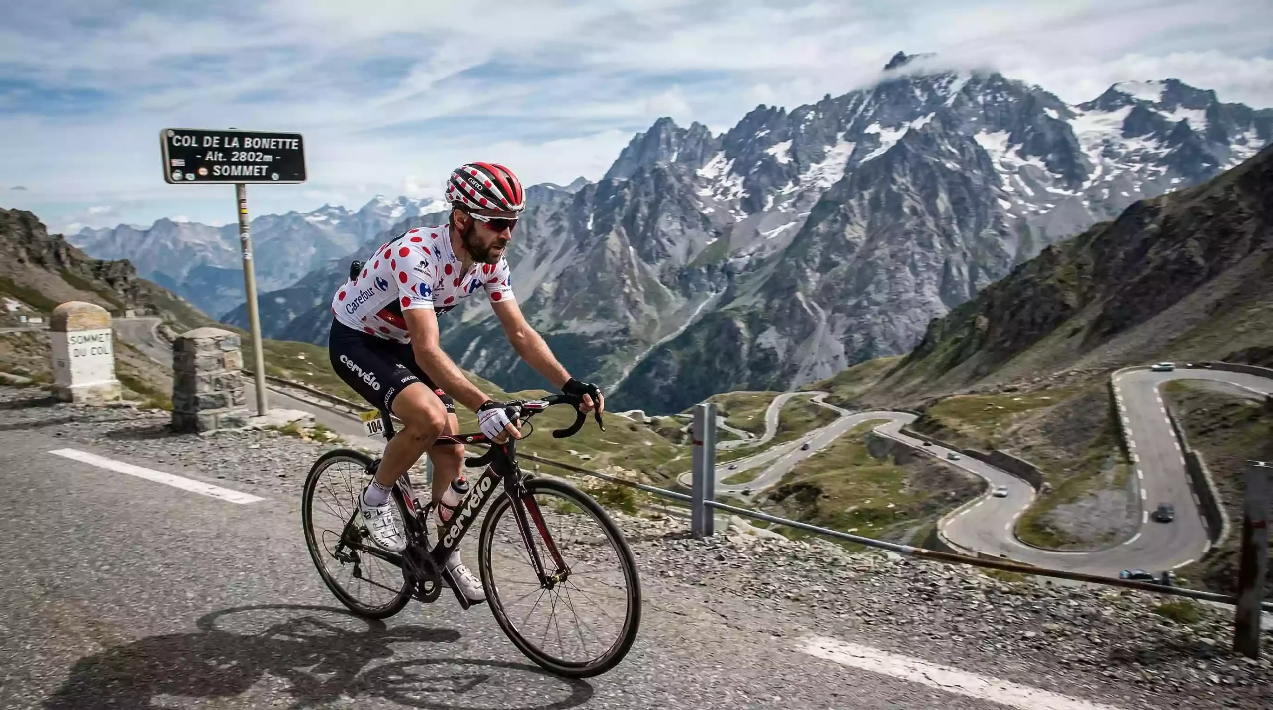 Ciclista escalador coronando un puerto de alta montaña con el maillot de lunares en una etapa de gran vuelta