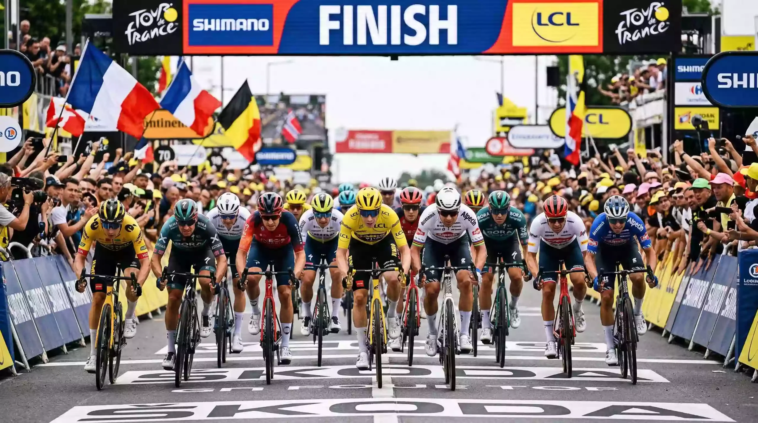 Pelotón de ciclistas en sprint masivo cruzando la línea de meta en una etapa llana de una gran vuelta